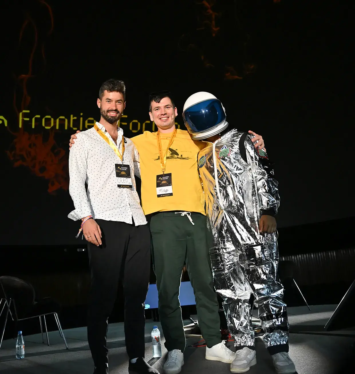 Two presenters on stage with a person in a silver astronaut suit