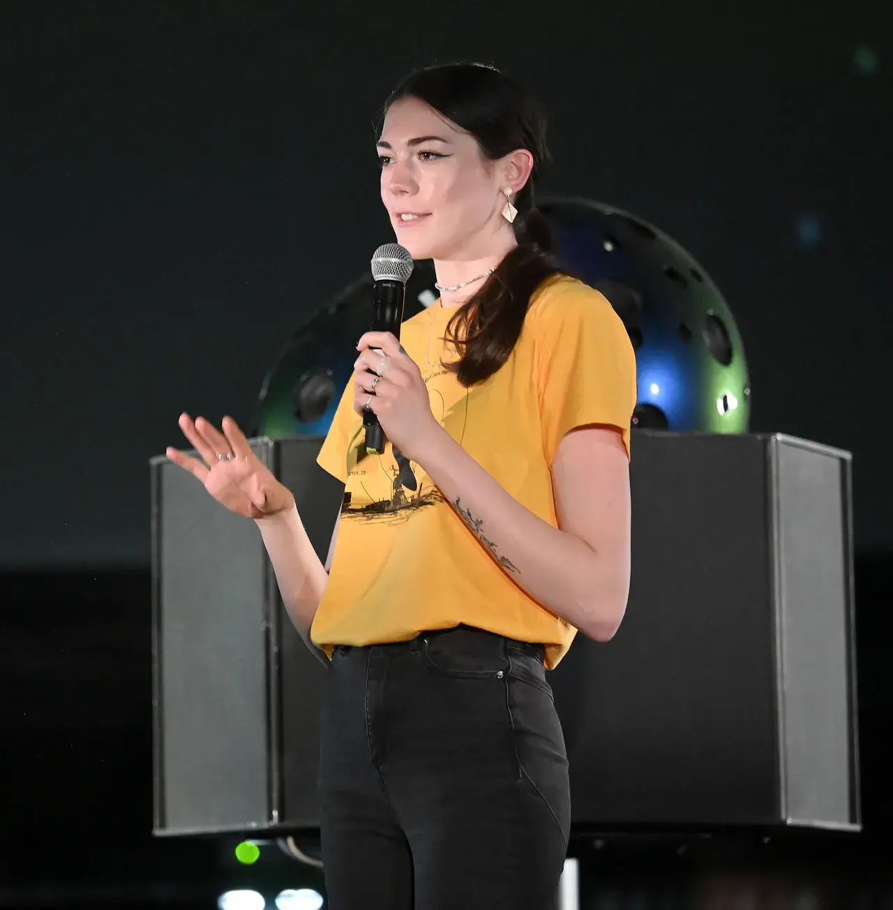 Speaker in a yellow SpaceComputer shirt presenting with a microphone